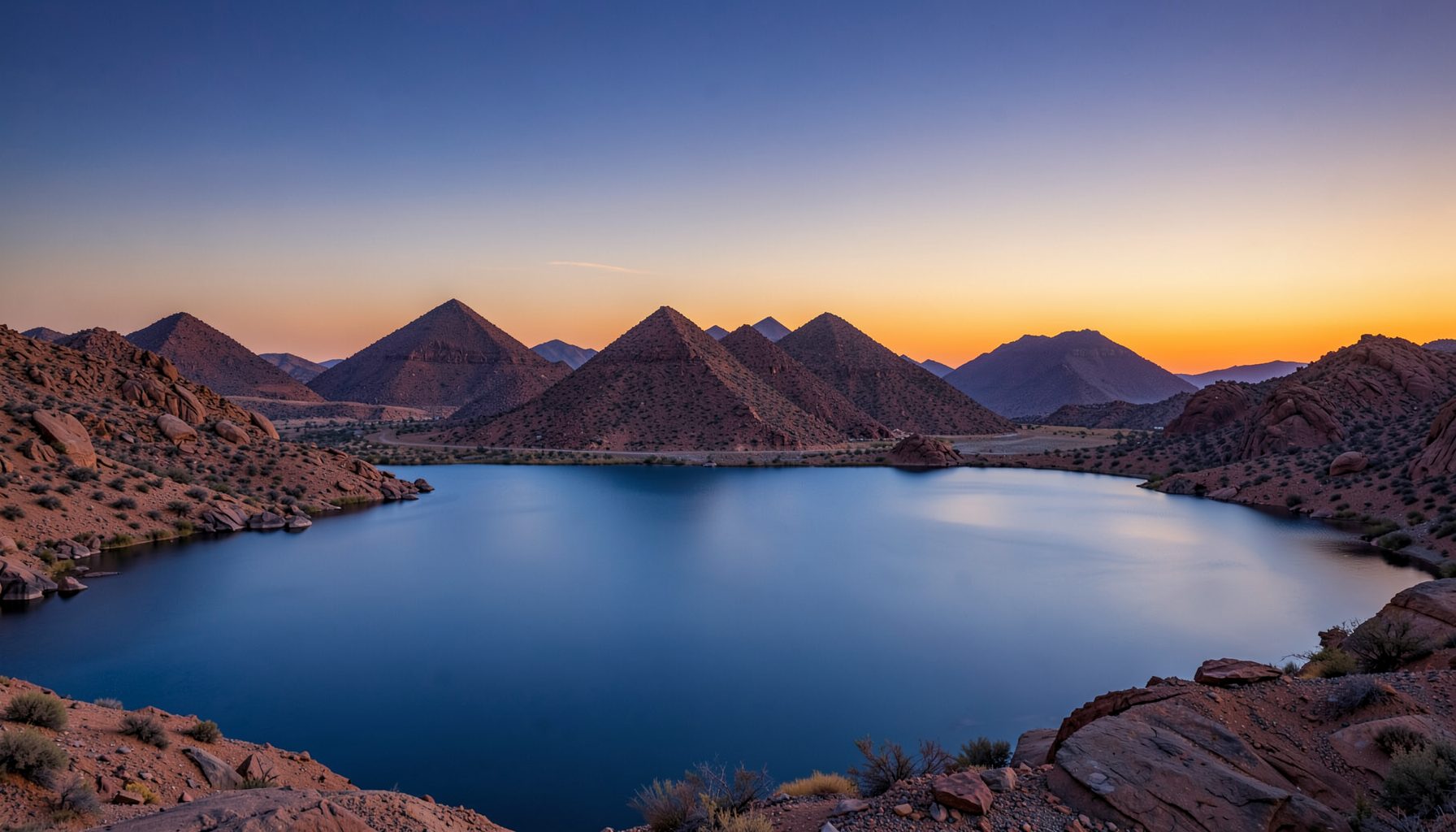 Pemandangan danau gurun yang luas dengan air biru tenang dan langit senja jingga keunguan, dikelilingi formasi batuan piramida khas Pyramid Lake
