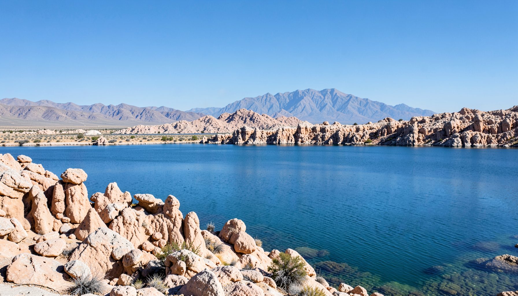 Pemandangan luas Pyramid Lake dengan air biru tenang, formasi batu tufa ikonik, dan langit biru cerah dengan pegunungan gurun di kejauhan